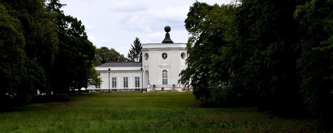 Na zdjęciu w tle Pałac w Jabłonnie, otoczony parkiem krajobrazowym z rozległym trawnikiem i drzewostanem