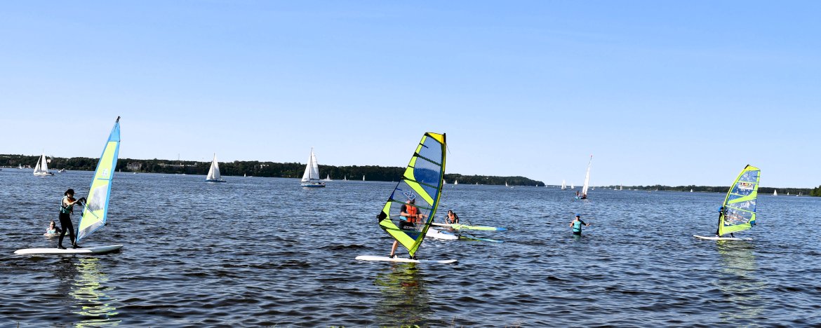 LSURF Szkoła Windsurfingu Kompleks Rekreacyjno - Wypoczynkowy Nieporęt Pilawa (ul. Aleja Wojska Polskiego 3). Osoby pływające na deskach windsurfingowych