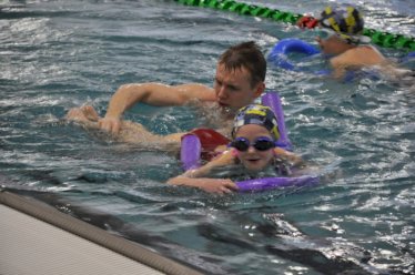 fot. www.trenujzmistrzami.com. Na zdjęciu mężczyzna uczy dziecko pływania w wodzie na basenie