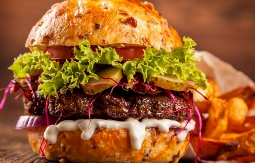 fot. facebook Serock Burger, www.facebook.com/Serock-Burger-1907031552954928/. Na zdjęciu burger z mięsem, sałatą, pomidorem, ogórkiem, czerwoną cebulą, sosem. Obok frytki