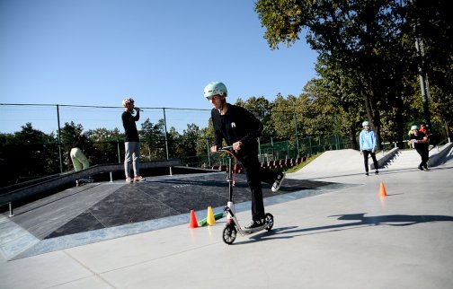 fot. Urząd Miasta Legionowo, www.legionowo.pl/a/stadion-miejski-w-legionowie. Na zdjęciu chłopak jedzie na hulajnodze na skateparku w Legionowie, z tyłu speaker trzyma mikrofon i coś mówi