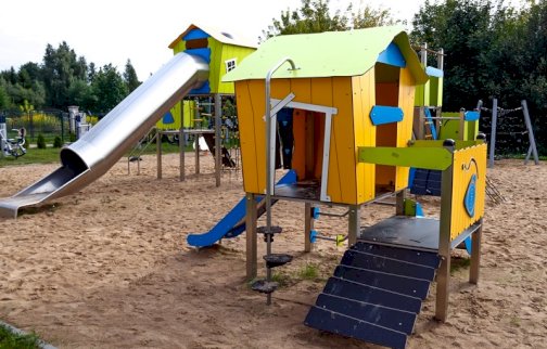 fot. sis.serock.pl. Na zdjęciu plac zabaw dla dzieci w Wierzbicy, zjeżdżalnia rurowa, płaska, domki dla dzieci, z tyłu po lewej stronie plenerowa siłownia zewnętrzna