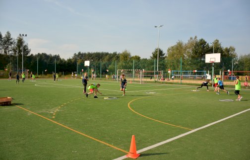 fot. https://www.nieporet.pl/sport-i-turystyka/obiekty-sportowe/. Na zdjęciu boisko wielofunkcyjne do gry w piłkę nożną, koszykową, w tle z tyłu boiska do gry w piłkę siatkową plażową, dzieci bawią się na boisku