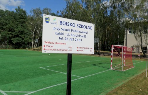 fot. splajski.edupage.org/. Na zdjęciu boisko do gry w piłkę nożną oraz koszykową, tablica informacyjna na temat boiska i telefonów alarmowych do służb