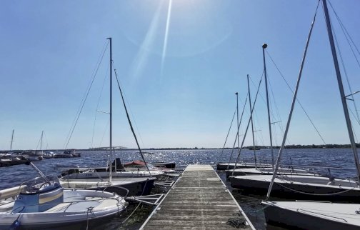 fot. zegrze360.pl. Na zdjęciu widok na pomost, łodzie żaglowe, motorowe po obu stronach pomostu, z tyłu woda