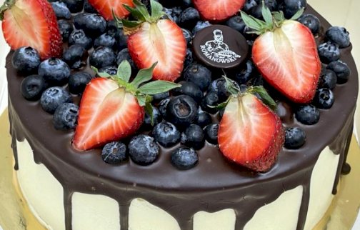 fot. https://www.cukierniaromanowski.pl. Na zdjęciu tort z borówkami i truskawkami z polewą czekoladową