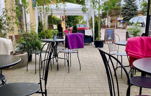 fot. www.slodkiebabki.com.pl. Na zdjęciu kawiarnia, stoliki z krzesełkami, w tle budynki mieszkalne, samochód osobowy po prawej stronie