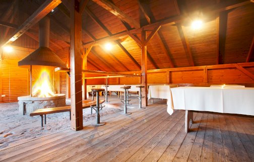 fot. http://geovita.pl/nasze-obiekty/jadwisin/. Na zdjęciu wiata grillowa, palenisko - widoczny ogień, rozstawione przy palenisku ławki, stoły w tle