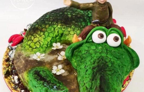fot. https://www.slodkiemarzenia.com. Na zdjęciu tort w kształcie smoka, na smoku siedzi uśmiechnięty chłopiec