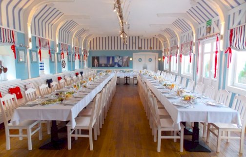 Powiększ obraz: fot. www.klubmila.pl/klub-mila-zegrzynek/restauracja. Na zdjęciu restuaracja Kapitańska Klub Mila w Zegrzynku, długie stoły z krzesłami