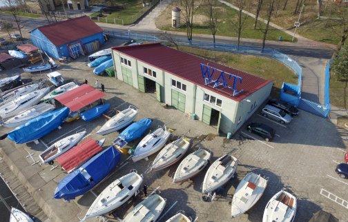 fot. www.wojsko-polskie.pl/wat/osrodek-szkoleniowy-w-zegrzu/. Na zdjęciu port z łodziami, hangar z napisem WAT, parking dla samochodów