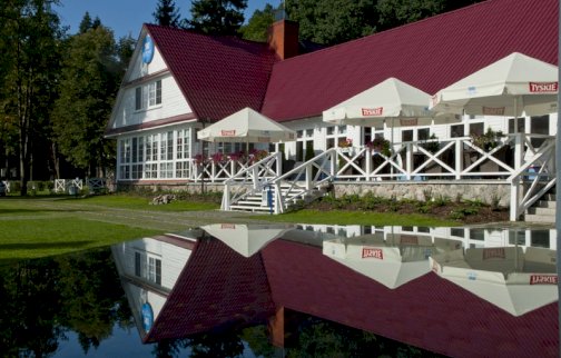 fot. www.klubmila.pl. Na zdjęciu Hotel Klub Mila w Zegrzynku, odbicie w lustrze wody hotelu, zielony trawnik, schody prowadzące do hotelu