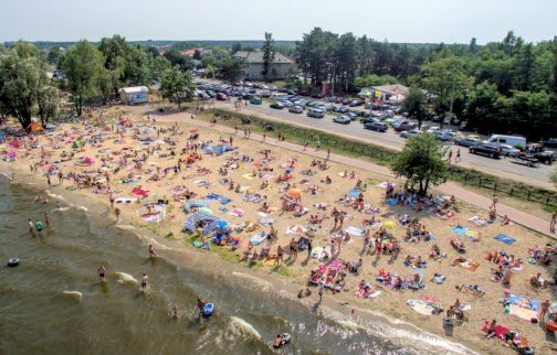 fot. www.water-club.pl. Na zdjęciu plaża, na której odpoczywają osoby na piasku, w tle samochody