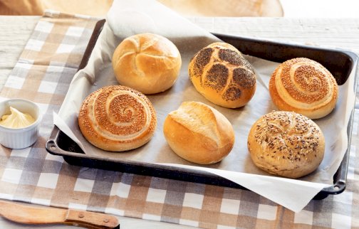 fot. www.facebook.com/SPCSmacznegoWarszawo/photos/?ref=page_internal. Na zdjęciu pieczone bułki na blacie do pieczenia, drewniany nożyk, w miseczce masło