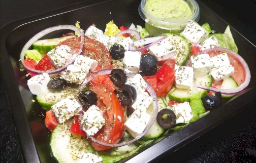 fot. facebook Look-Cook Catering, www.facebook.com/LOOKCOOKCatering/?ref=page_internal. Na zdjęciu sałatka z pomidorami, serem, czarnymi oliwkami, czerwoną cebulą  w czarnym plastikowym pojemniku, obok zielony sos w pudełeczku