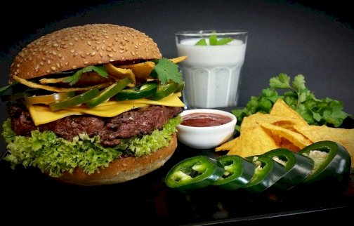 fot. www.beef-burger.pl/.  Na zdjęciu burger z mięsem, papryczką, sałatą, pietruszką, serem żółtym, obok sosy