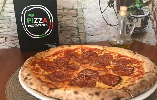 fot. www.przystanekpizza.eu/galeria. Na zdjęciu pizza z salami, serem żółtym, karta menu PIZZA PRZYSTANEK, oliwa z oliwek w butelce