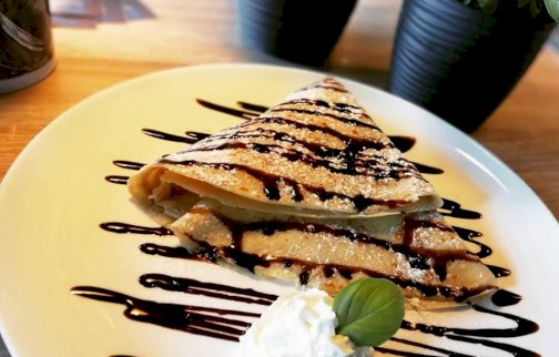 fot. Naleśnikarnia plackarnia Legionowo, www.plackarnialegionowo.pl/. Na zdjęciu naleśnik w polewie czekoladowej z bitą śmietaną