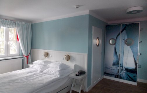 fot. www.klubmila.pl. Na zdjęciu pokój sypialny z łóżkiem, krzesełko obok łóżka, po prawe stronie drzwi wejściowe do pokoju