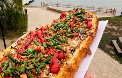 fot. restauracja Zapiekane Niebo w Gębie. Na zdjęciu zapiekanka, widok na Zalew Zegrzyński, ścieżkę pieszo - rowerową, z przodu pomost, w oddali na jeziorze osoby pływają na łodzi