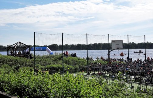 fot. Krzysztof Kozań. Boisko do gry w piłkę koszykową o sztucznej nawierzchni obok plaży miejskiej w Serocku, na boisku stoją rowery, w tle z tyłu ludzie stojący nad wodą, rzeka Narew w Serocku