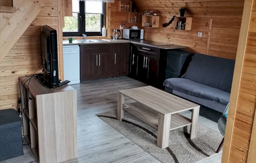 fot. www.dzikizakatekpiskornia.pl. Na zdjęciu domek nad Narwią w Dzierżeninie, sofa, w środku pokoju stolik, po lewej stronie na szafce telewizor, schody prowadzące na piętro