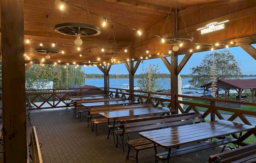 fot. facebook Tawerna Cicha Zatoka w Wierzbicy nad Narwią, https://www.facebook.com/profile.php?id=61564926346648. Na zdjęciu stoliki z ławkami pod zadaszeniem, w tle rzeka Narew