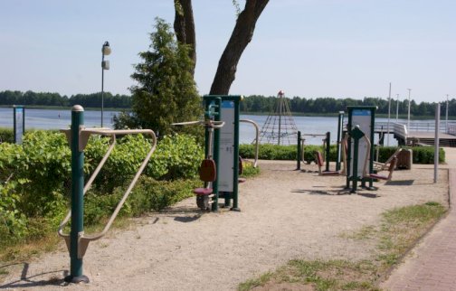 fot. https://sis.serock.pl/5234,silownia-zewnetrzna. Na zdjęciu siłownia plenerowa w Serocku na plaży miejskiej w Serocku, w tle rzeka Narew, molo miejskie w Serocku