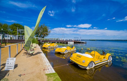 fot. Robert Małecki FOTOGRAFIA, www.hotel500.com.pl/zegrze/galeria. Na zdjęciu na wodzie żółte rowerki wodne, leżaki, fragment plaży, molo