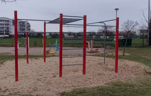 fot. Krzysztof Kozań. Na zdjęciu stacja drążków do podciągania, w tle budynki mieszkalne, urządzenia zabawowe dla dzieci, boisko do piłki nożnej z bramkami