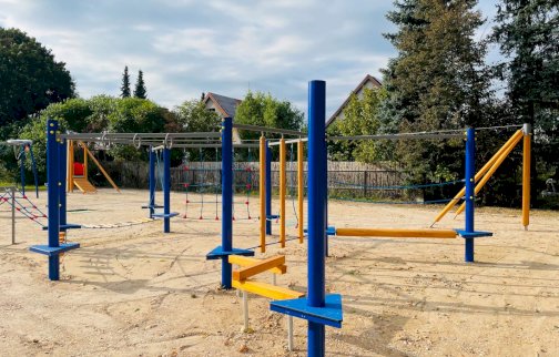 fot. www.nieporet.pl/inwestycje-gminne/inwestycje-2021/ogrod-rybaka/46212/. Na zdjęciu prace przy montażu Ogrodu Rybaka w Nieporęcie. Plac zabaw dla dzieci, linarium, w tle z tyłu tyrolka dla dzieci, podesty do przechodzenia