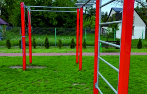 fot. https://serock.pl/54-serock-silownia-plenerowa-w-stasim-lesie. Na zdjęciu drążki do podciągania, drabinka pozioma, w tle budynki mieszkalne