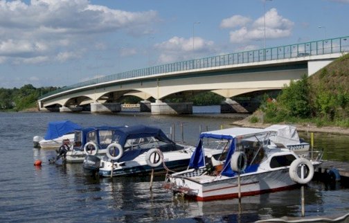 fot. Przystań Przy Starym Moście, https://ppsm.pl/galeria/#bwg1/18. Na zdjęciu zacumowane łodzie, z tyłu most w Zegrzu, Jezioro Zegrzyńskie