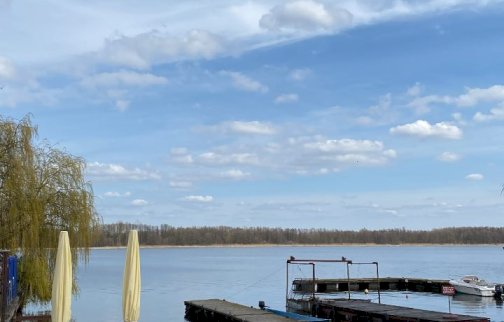 fot. facebook Tawerna Cicha Zatoka w Wierzbicy nad Narwią, https://www.facebook.com/photo?fbid=122154414026497544&set=a.122110949342497544. Na zdjęciu pomosty na rzece Narwi, łódź, zwinięte parasole, zielony trawnik na terenie obiektu