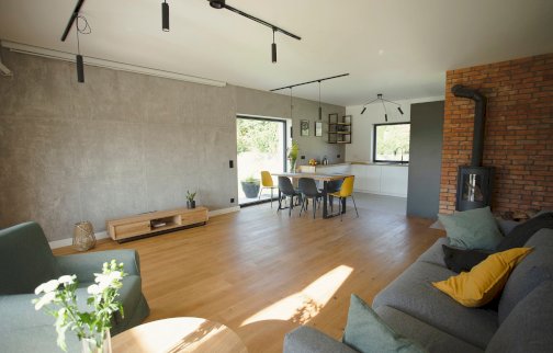 fot. facebook Dom na Cuplu, https://www.facebook.com/photo/?fbid=276068737850650&set=pcb.276070777850446. Na zdjęciu salon z kominkiem, stół z krzesłami, fotel, kanapa