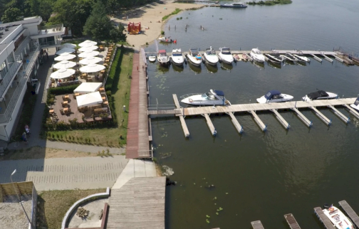 fot. www.marinadiana.pl. Na zdjęciu port Hotelu Marina Diana w Białobrzegach, po lewej stronie budynek hotelowy, ogródek z parasolami na zewnątrz, z tyłu piaszczysta plaża