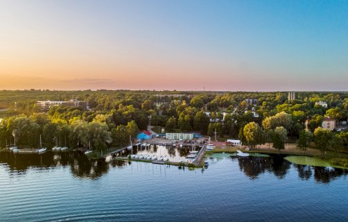 fot. Ośrodek Szkoleniowy WAT Zegrze. Na zdjęciu Ośrodek Szkoleniowy WAT Zegrze, w basenie portowym łodzie żaglowe, widoczny fragment Jeziora Zegrzyńskiego. W tle lasy, zabudowania mieszkalne