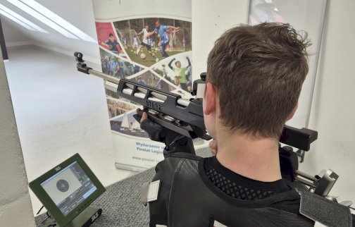 Fot. Tomasz Zatoń. Na zdjęciu chłopiec celuje z broni pneumatycznej. Poniżej na stoliku ekran prezentujący tarczę. W tle roll up