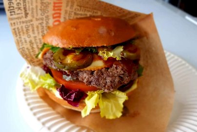 Powiększ obraz: fot. facebook Bistro u Miśków, https://www.facebook.com/profile.php?id=100063485915346. Na zdjęciu burger z mięsem, ogórkiem, czerwoną sałatą, burger zawinięty w papierze