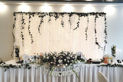 Powiększ obraz: fot. bukowiec.eu. Na zdjęciu ozdobiona firanka, stół - napis "Mąż żona". Uroczystość weselna dla pary młodej