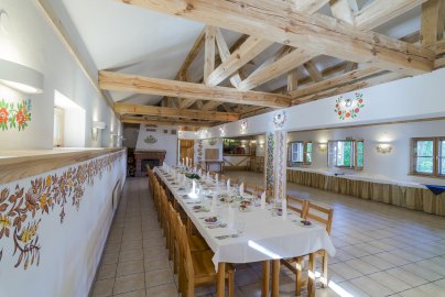 Powiększ obraz: fot. geovita.pl/nasze-obiekty/jadwisin/. Na zdjęciu długa sala, stół zakryty obrusem z krzesełkami, zastawa stołowa, talerzyki, sztućce - noże, widelce, łyżki na stole
