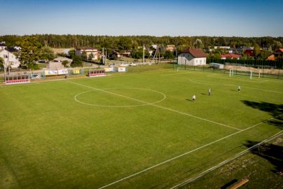 Powiększ obraz: fot. osir.nieporet.pl/info/zawartosc/67/. Na zdjęciu boisko trawiaste do gry w piłkę nożną, piłkarze trenują na murawie  piłkarskiej, w tle domy mieszkalne