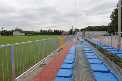 Powiększ obraz: fot. https://cr.nieporet.pl/info/zawartosc/67/. Na zdjęciu trybuny piłkarskie, po lewej stronie fragment murawy piłkarskiej, w tle domy mieszkalne