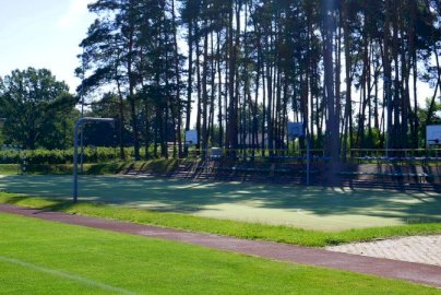 Powiększ obraz: fot. sis.serock.pl/3926,boisko. Na zdjęciu boisko do gry w koszykówkę z koszami, w tle bramka do piłki nożnej, brązowa bieżnia do biegów, w tle trybuny złożone z krzesełek