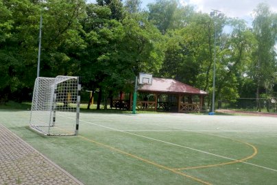 Powiększ obraz: fot. sis.serock.pl/3836,nowa-wies. Na zdjęciu boisko do gry w piłkę nożną, po lewej stronie zdjęcia bramka z siatką do gry w piłkę nożną, w tle tablica do koszykówki, boisko do piłki siatkowej, drewniana wiata