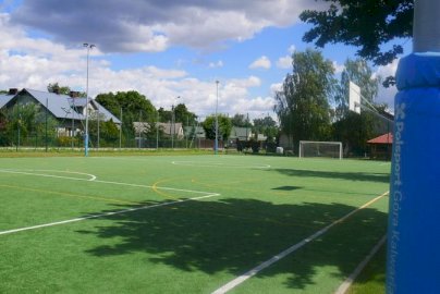 Powiększ obraz: fot. sis.serock.pl/3838,gasiorowo. Na zdjęciu boisko o sztucznej  nawierzchni do gry w piłkę koszykową oraz piłkę nożną, w tle domy mieszkalne