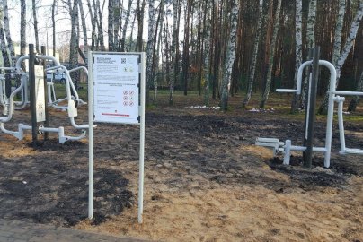 Powiększ obraz: fot. facebook Gmina Wieliszew, https://www.facebook.com/photo?fbid=1570592393024061&set=a.1570592213024079&locale=pl_PL. Na zdjęciu siłownia plenerowa na Osiedlu 600 - lecia w Wieliszewie, tablica wraz z regulaminem, w tle drzewa - brzozy