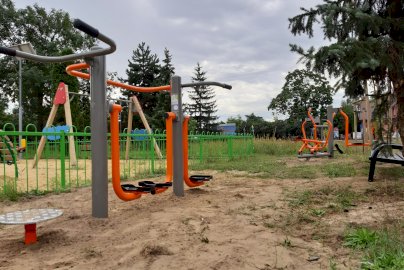 Powiększ obraz: fot. www.nieporet.pl/spolecznosc-gminna/nowe-silownie-plenerowe/. Na zdjęciu siłownia plenerowa w Stanisławowie Pierwszym: biegacz, twister, wahadło, w tle plac zabaw dla dzieci