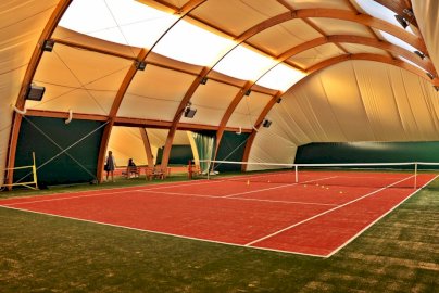 Powiększ obraz: fot. tenis-legionowo.pl. Na zdjęciu w hali kort do tenisa ziemnego, po lewej stronie jedna z osób stoi, a druga siedzi na ławce