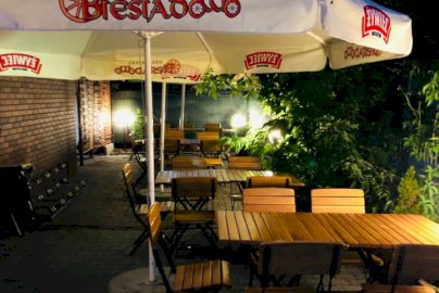 Powiększ obraz: fot. Pizzeria Biesiadowo Legionowo, https://www.facebook.com/biesiadowolegionowo. Na zdjęciu drewniane stoliki z krzesłami, parasol z napisem SIEĆ PIZZERI BIESIADOWO, napis na dole Perfect